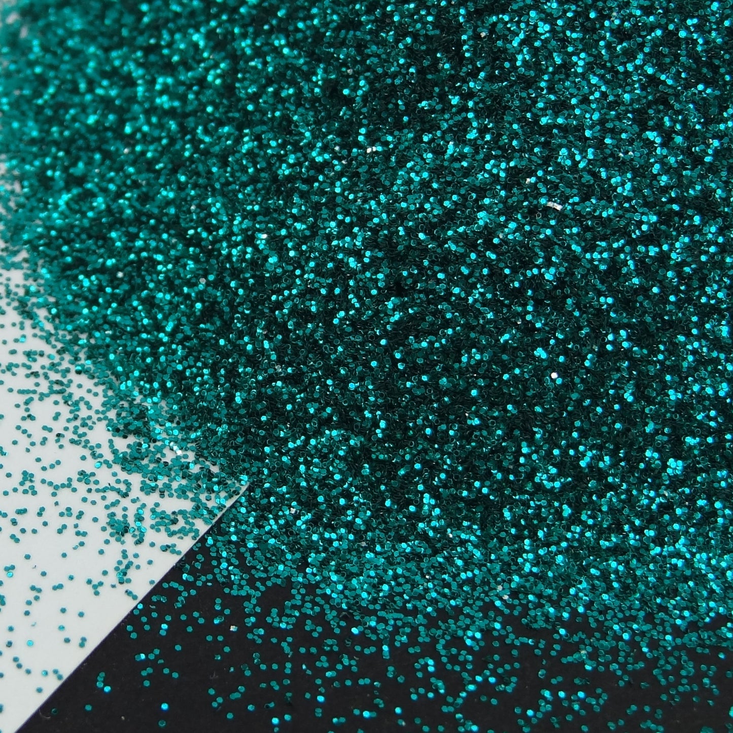 A turquoise extra fine glitter spread out on a black and white background.