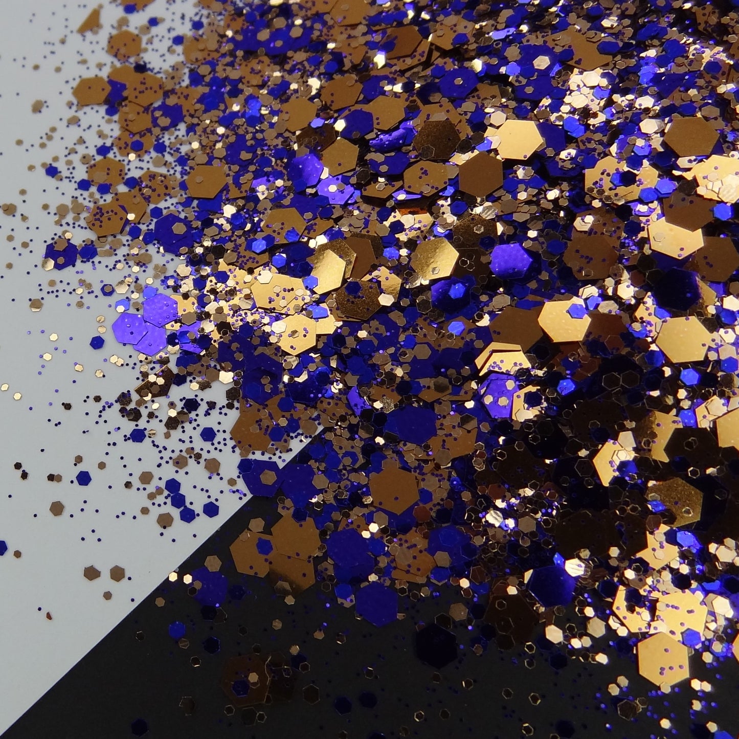 A pile of mixed colours of chunky glitter, including Indigo/Bronze, on a white and black background.