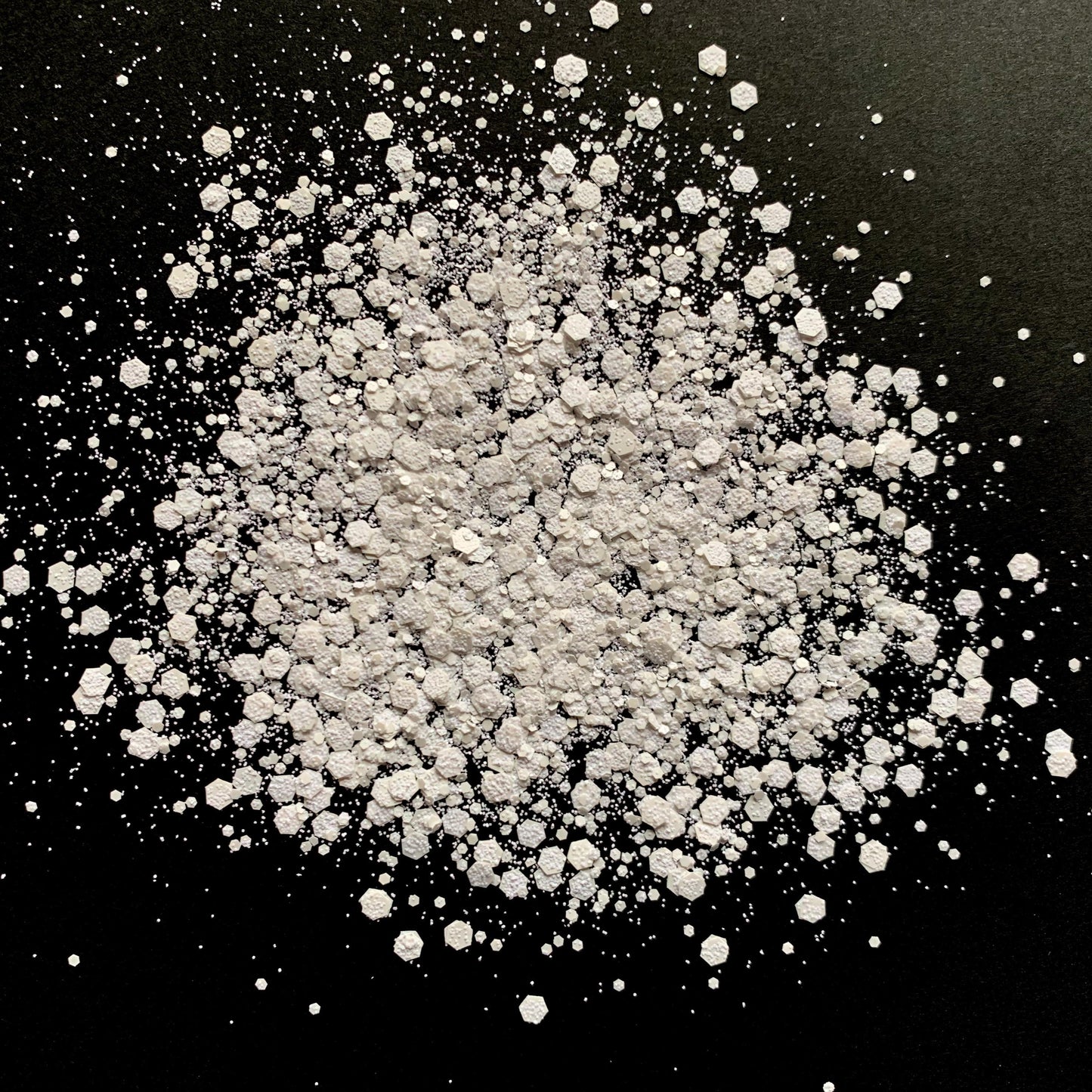 A pile of white chunky glitter on a black background