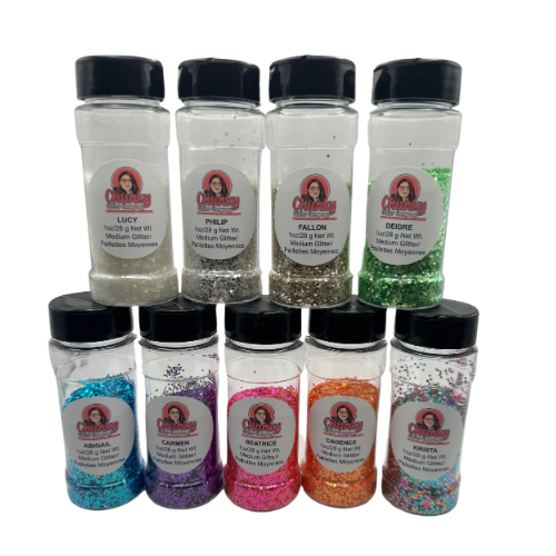 A collection of nine jars of glitter in various colors, labeled with names such as 'Philip' and 'Lucy', intended for use in snowglobe tumblers.