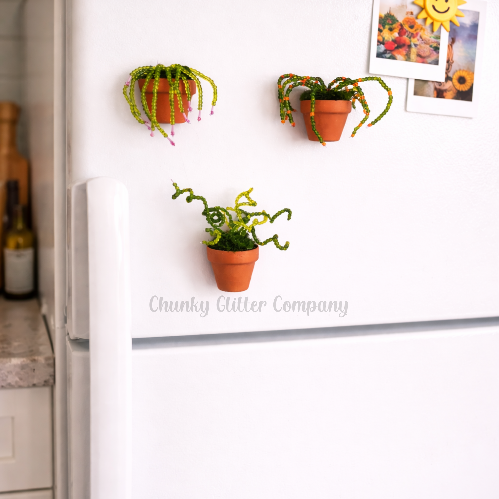 Three beaded plants turned into magnets attached to a refrigerator.