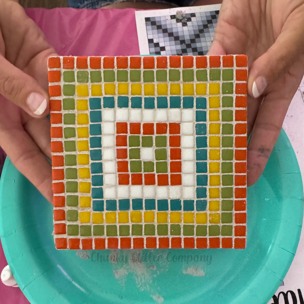 Colorful mosaic square held by hands on a teal plate
