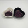 Two heart-shaped dishes, one white and one black, containing dark glitter.