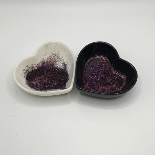 Two heart-shaped dishes, one white and one black, containing dark glitter.