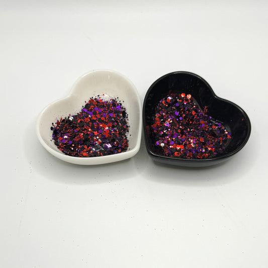 Two heart shaped containers, one black, one white, containing a Red/White/Blue/Silver chunky glitter mix with hexagons, snowflakes and stars.