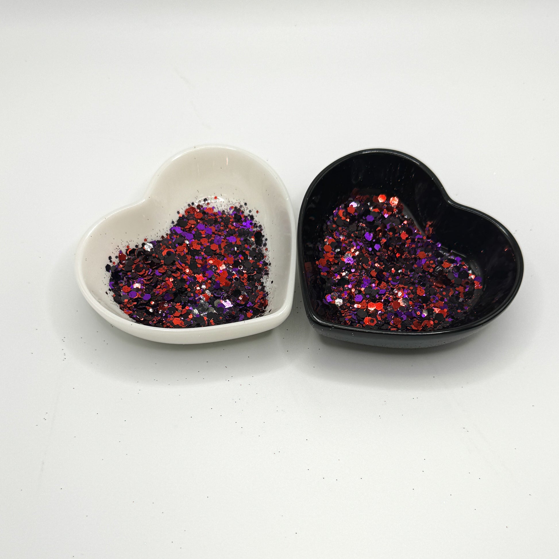 Two heart shaped containers, one black, one white, containing a Black/Red/Purple chunky glitter mix.