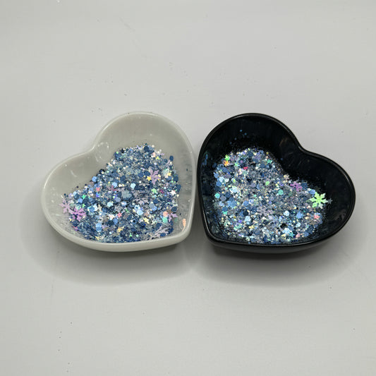 Two heart shaped containers, one black, one white, containing a Blue/White/Rainbow/Silver chunky glitter mix with hexagons, snowflakes and stars.