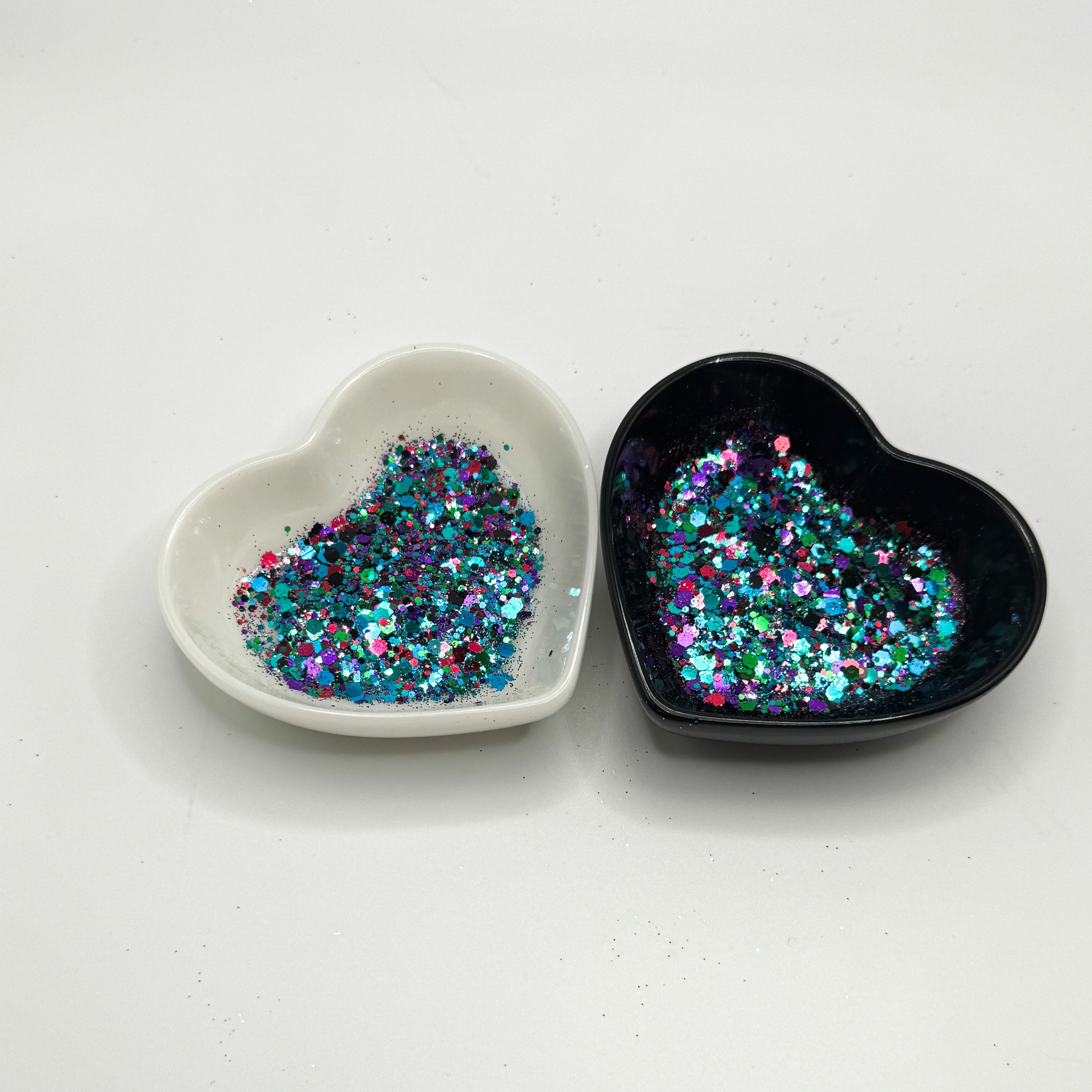 Two heart shaped containers, one black, one white, containing a Green/Black/Purple/Pink/Teal/Blue chunky glitter mix.
