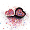 Two heart shaped containers, one black, one white, containing a Red/Purple/Rainbow chunky glitter mix.
