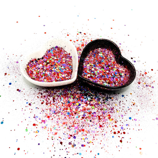Two heart shaped containers, one black, one white, containing a Red/Purple/Rainbow chunky glitter mix.