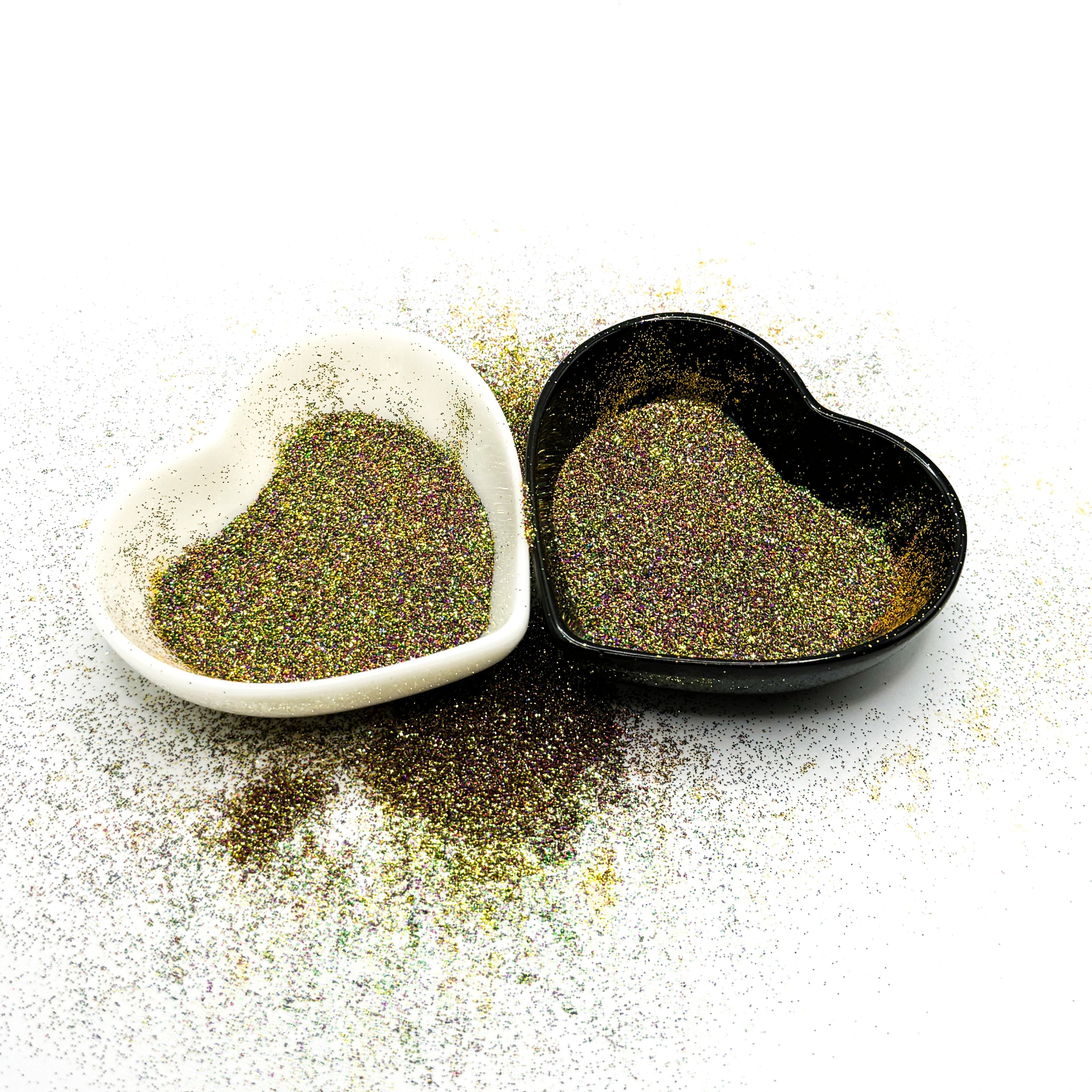 Two heart-shaped containers of glitter, one black and the other white, both showing an extra fine, green, purple glitter mix