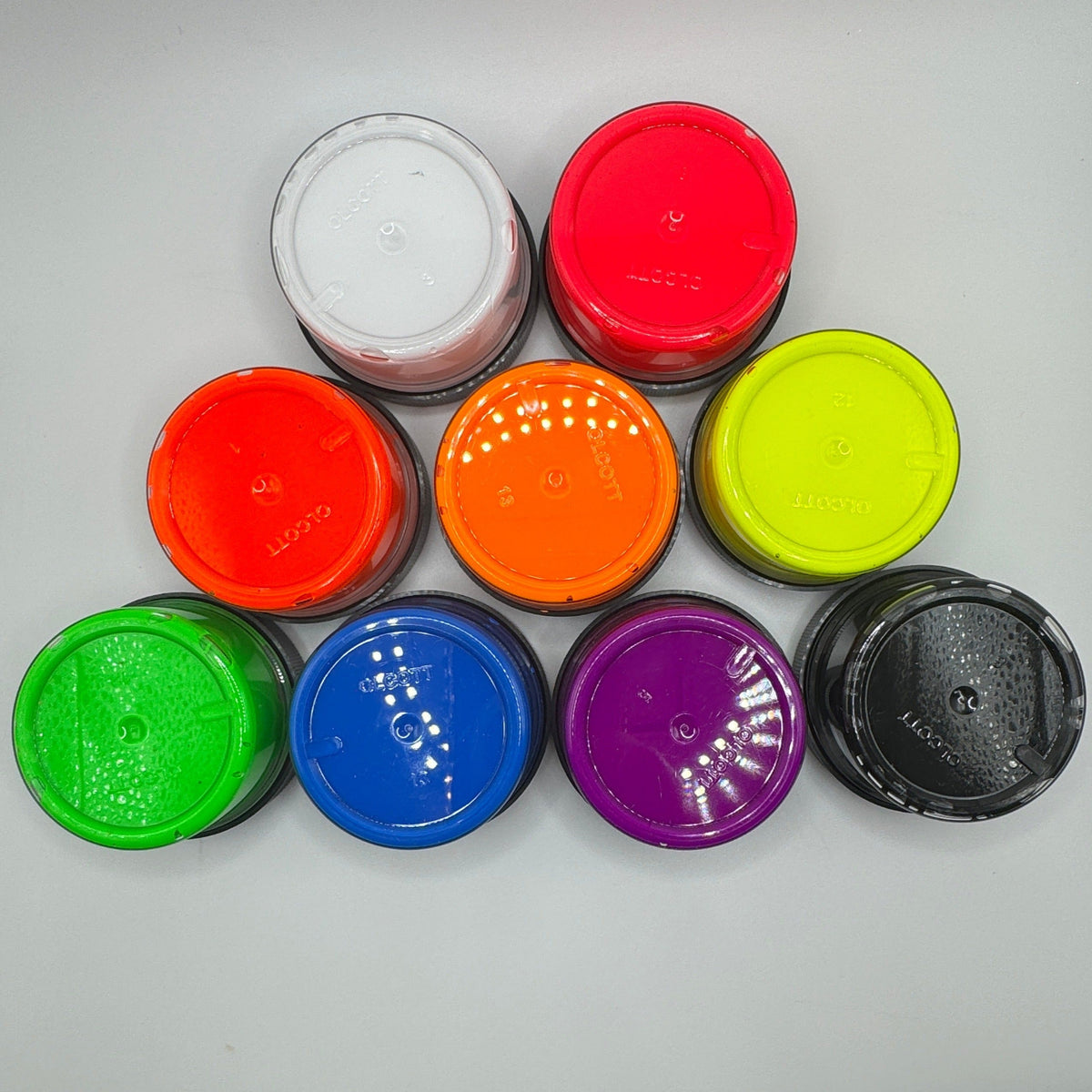 An assortment of nine pigment paste pots in various colors including white, coral, orange, yellow, green, blue, purple, and black.