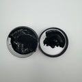 A jar of black pigment paste open with the pigment visible, placed on a white surface.