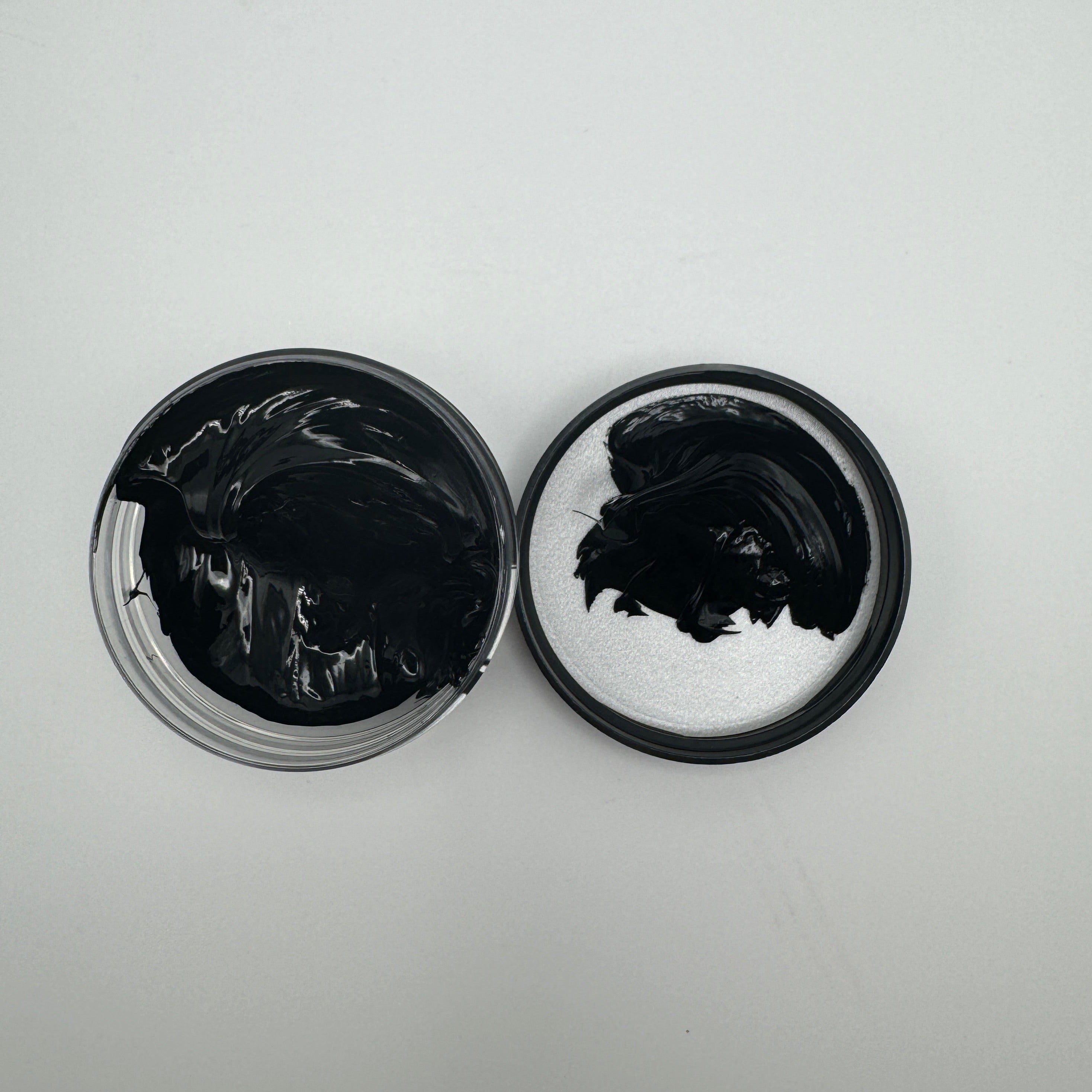 A jar of black pigment paste open with the pigment visible, placed on a white surface.