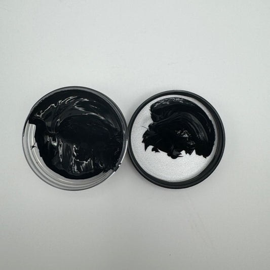 A jar of black pigment paste open with the pigment visible, placed on a white surface.