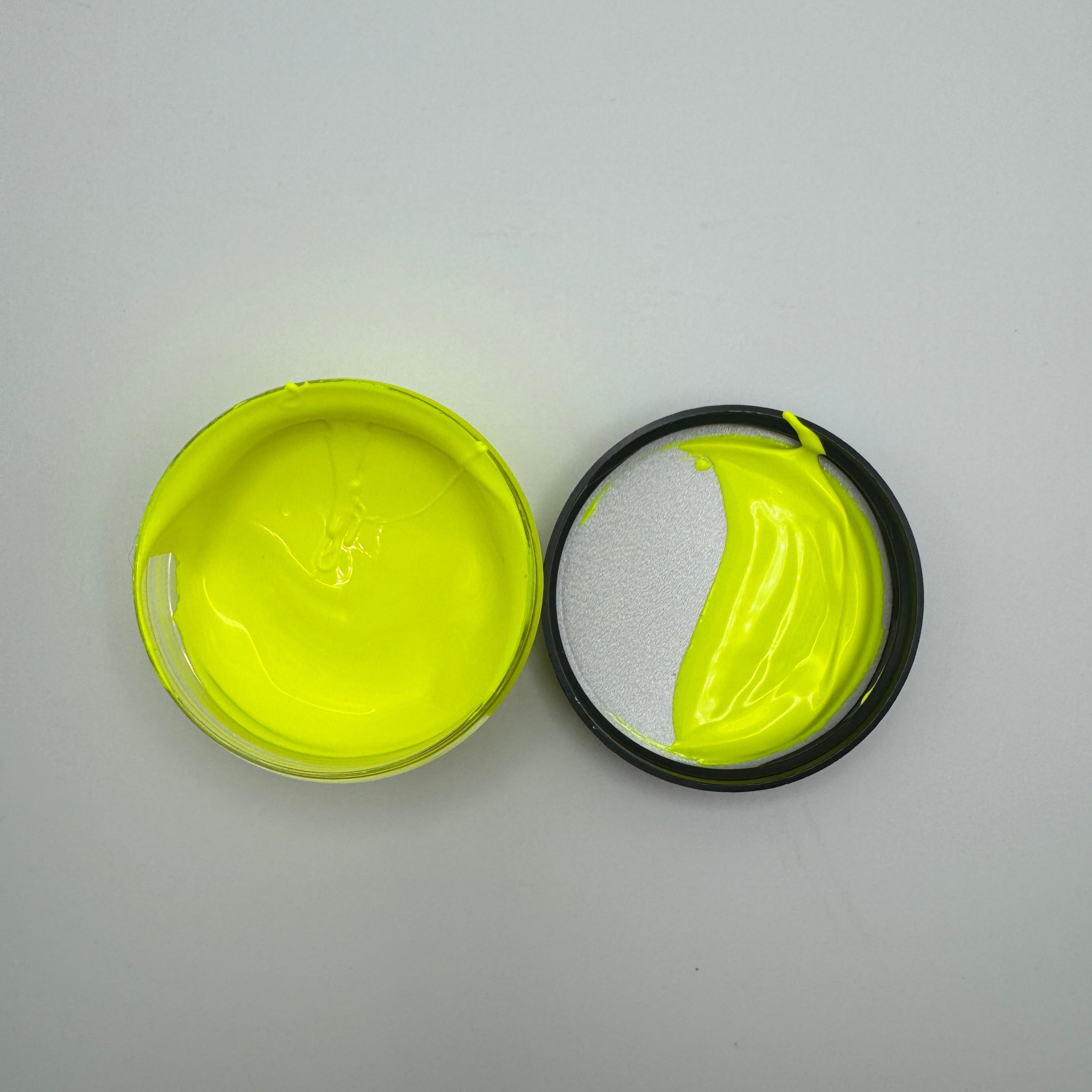 A jar of electric yellow pigment paste opened and showing the bright yellow color, placed on a white surface.