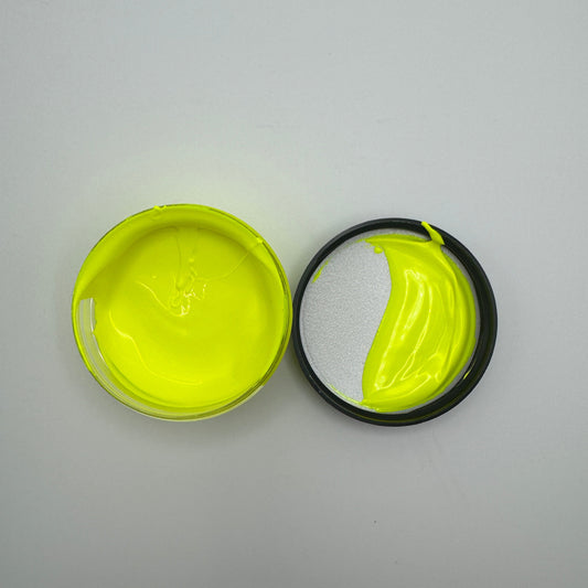 A jar of electric yellow pigment paste opened and showing the bright yellow color, placed on a white surface.