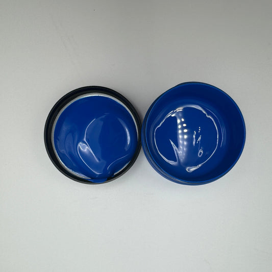 Two small open jars with blue pigment paste, viewed from above on a white background.