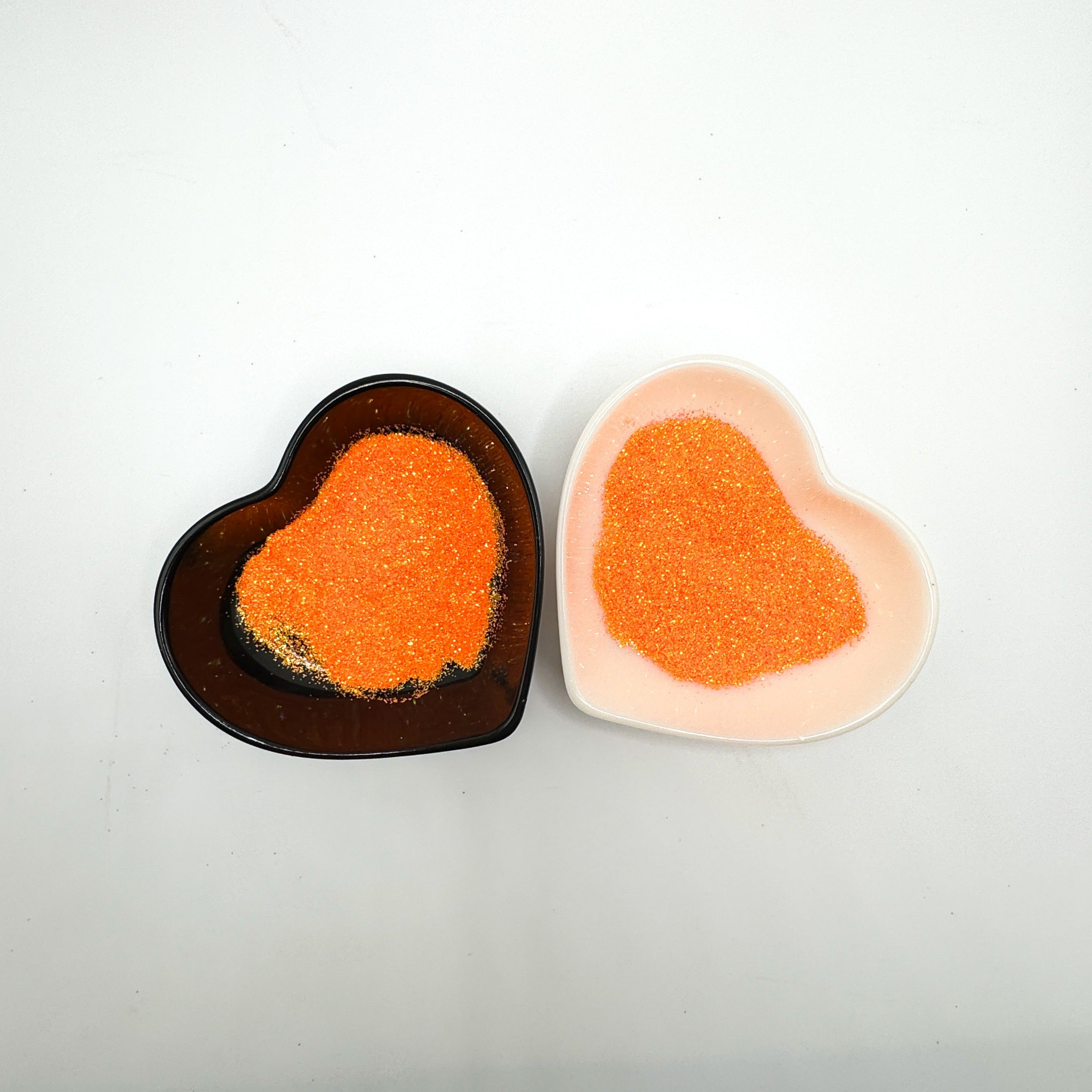 Two heart-shaped containers of glitter, one black and the other white, both showing an extra fine, orange glitter mix