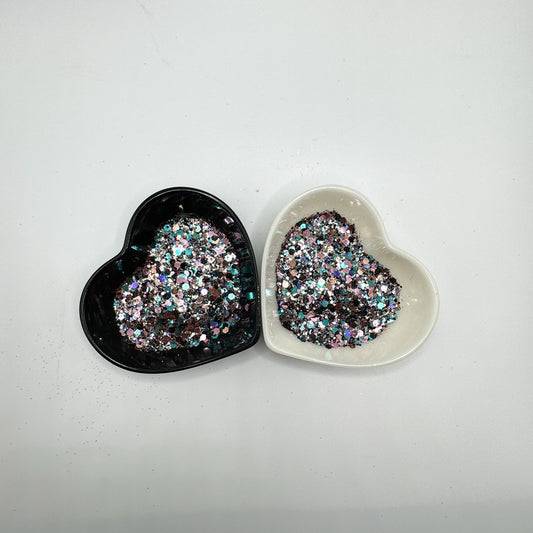 Two heart shaped containers, one black, one white, containing a Blue/Black/Light Teal/Rose Gold/Light Pink chunky glitter mix.