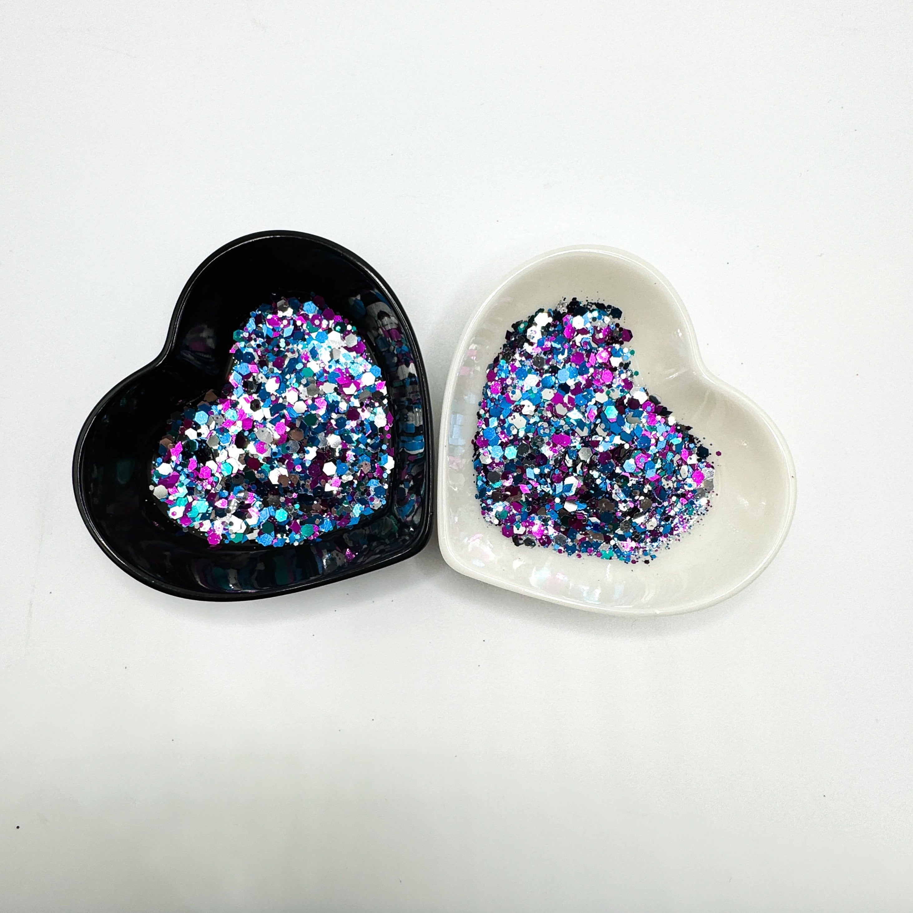 Two heart shaped containers, one black, one white, containing a Black/Blue/Pink/White chunky glitter mix with hexagons and diamonds.