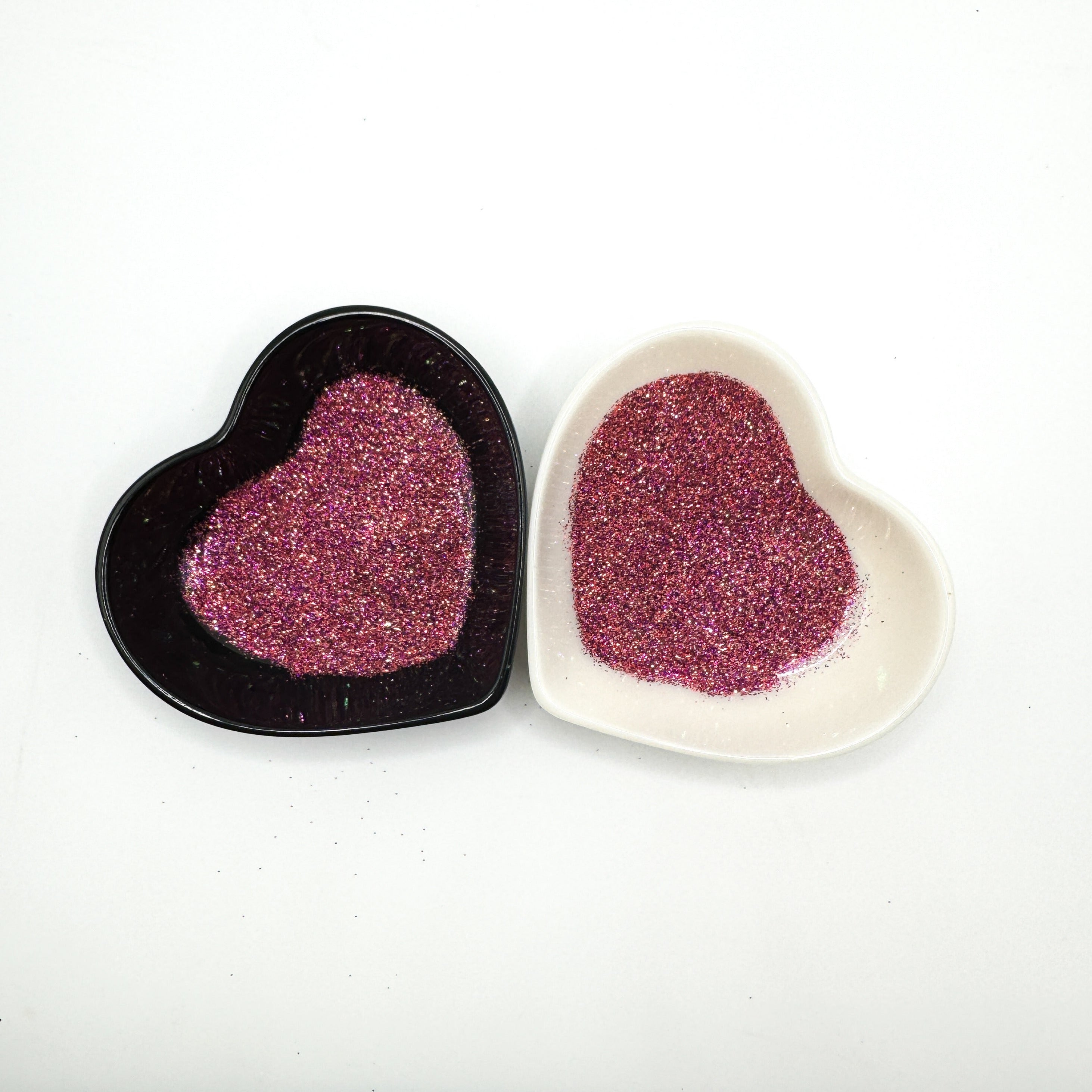 Two heart-shaped containers of glitter, one black and the other white, both showing an extra fine, pink multicoloured glitter mix