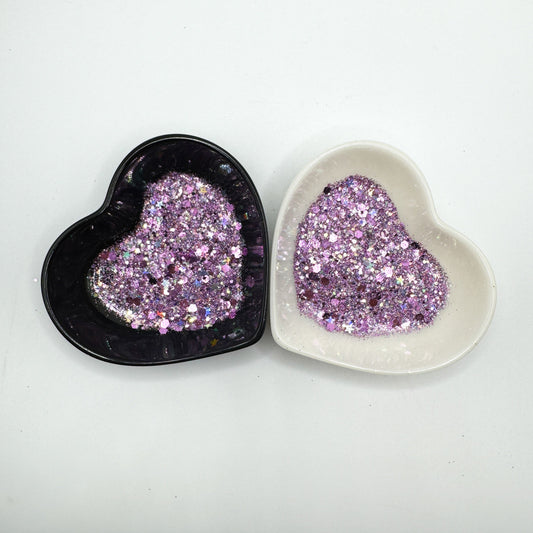 Two heart shaped containers, one black, one white, containing a Purple/Silver chunky glitter mix with hexagons and stars.