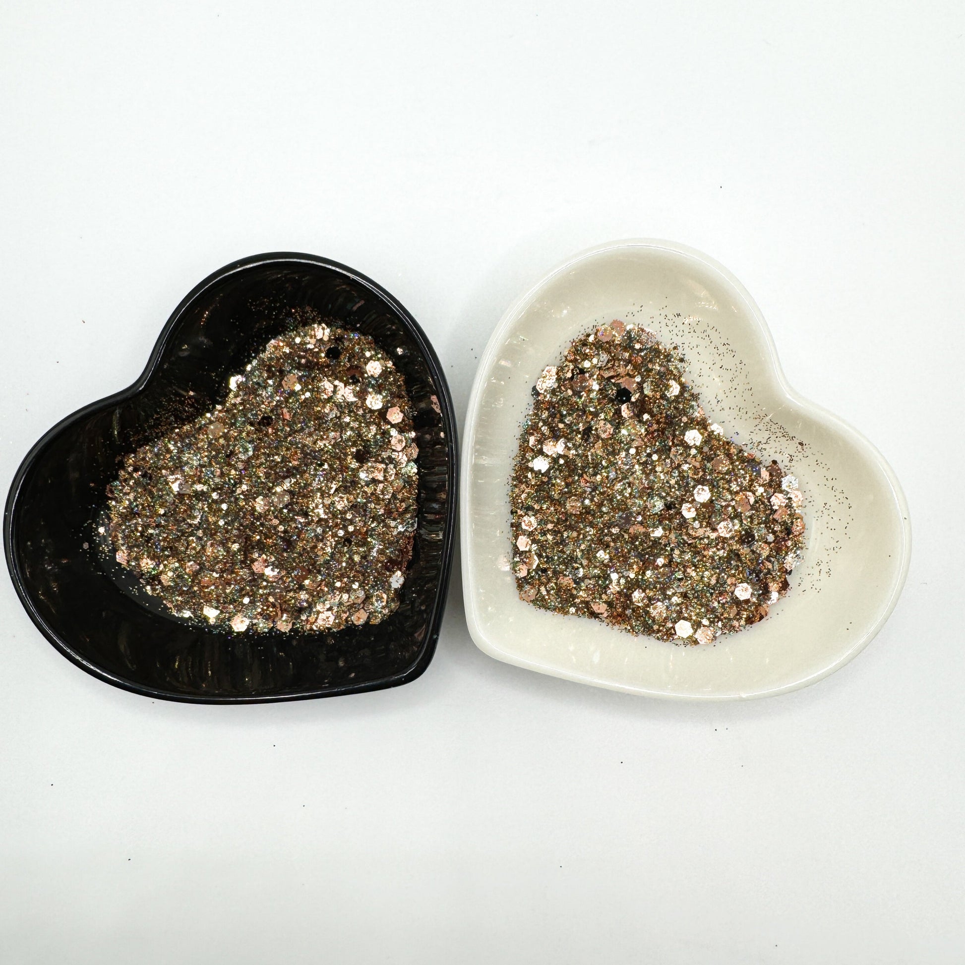 Two heart shaped containers, one black, one white, containing a Light Teal/Black/Silver/Rose Gold chunky glitter mix.