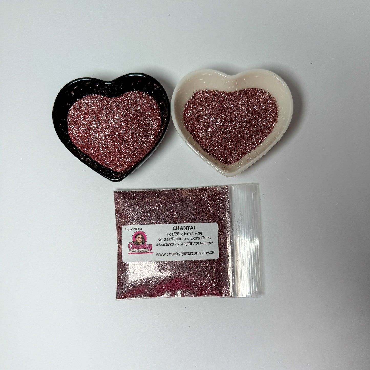 Two heart-shaped containers of glitter, one black and the other white, both showing an extra fine, dusty rose glitter mix and a bag of glitter with a label that reads Chantal.