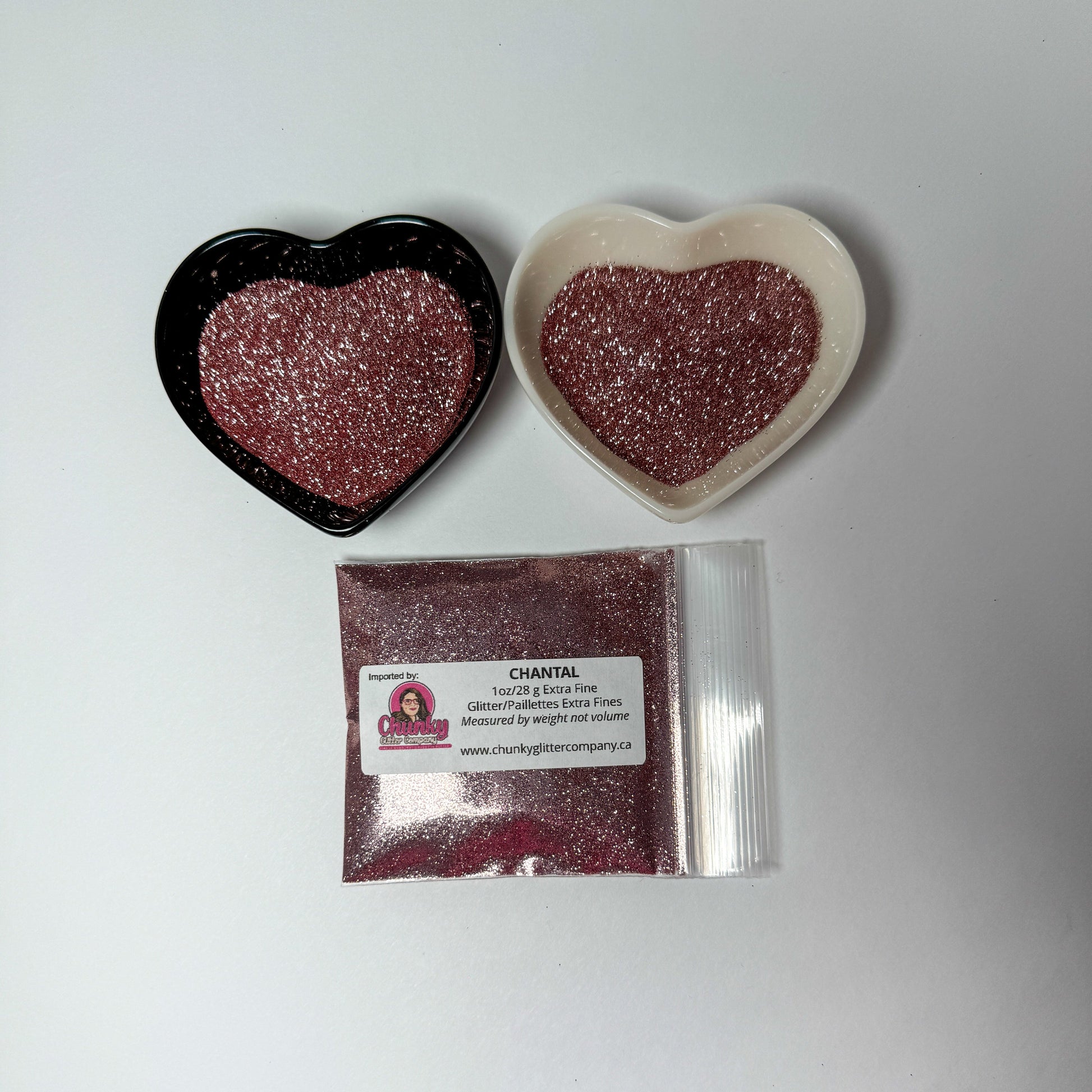 Two heart-shaped containers of glitter, one black and the other white, both showing an extra fine, dusty rose glitter mix and a bag of glitter with a label that reads Chantal.