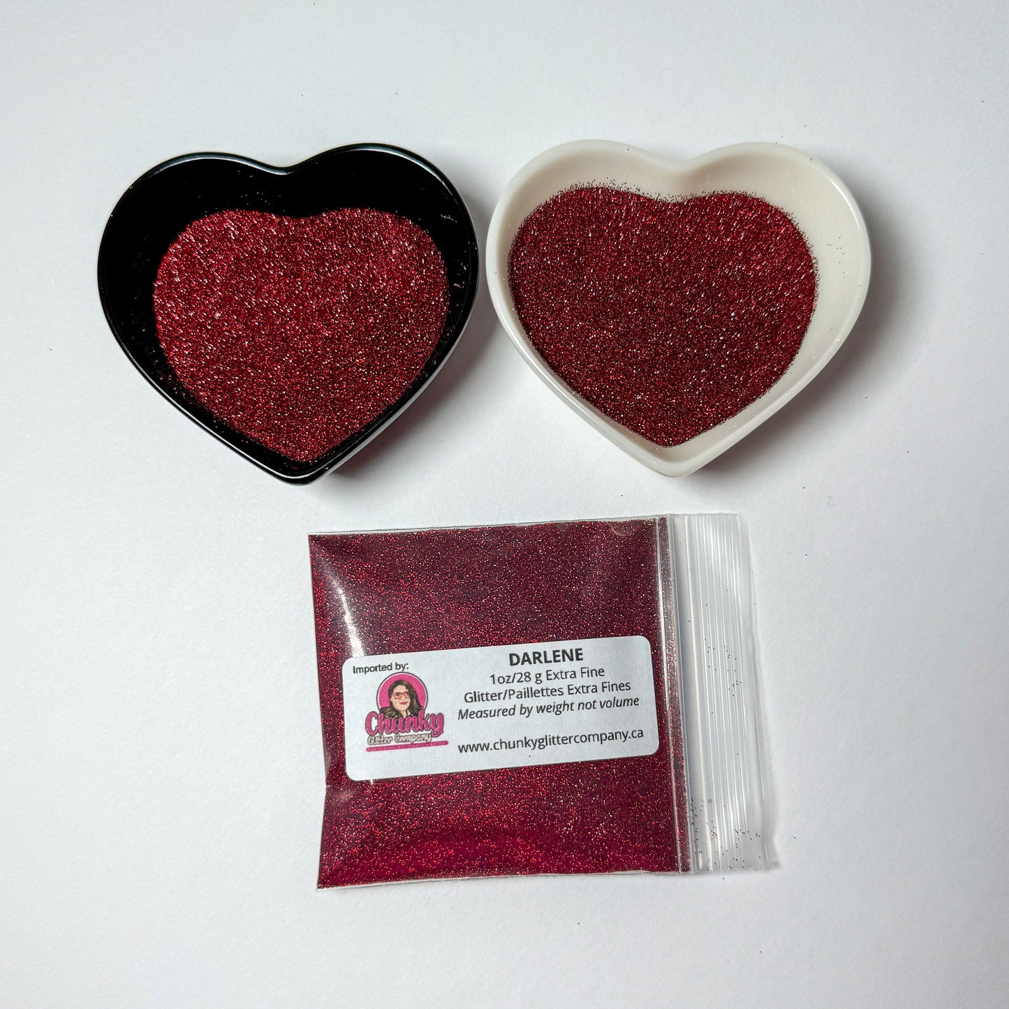 Two heart-shaped containers of glitter, one black and the other white, both showing an extra fine, maroon glitter mix and a bag of glitter with a label that reads Darlene.