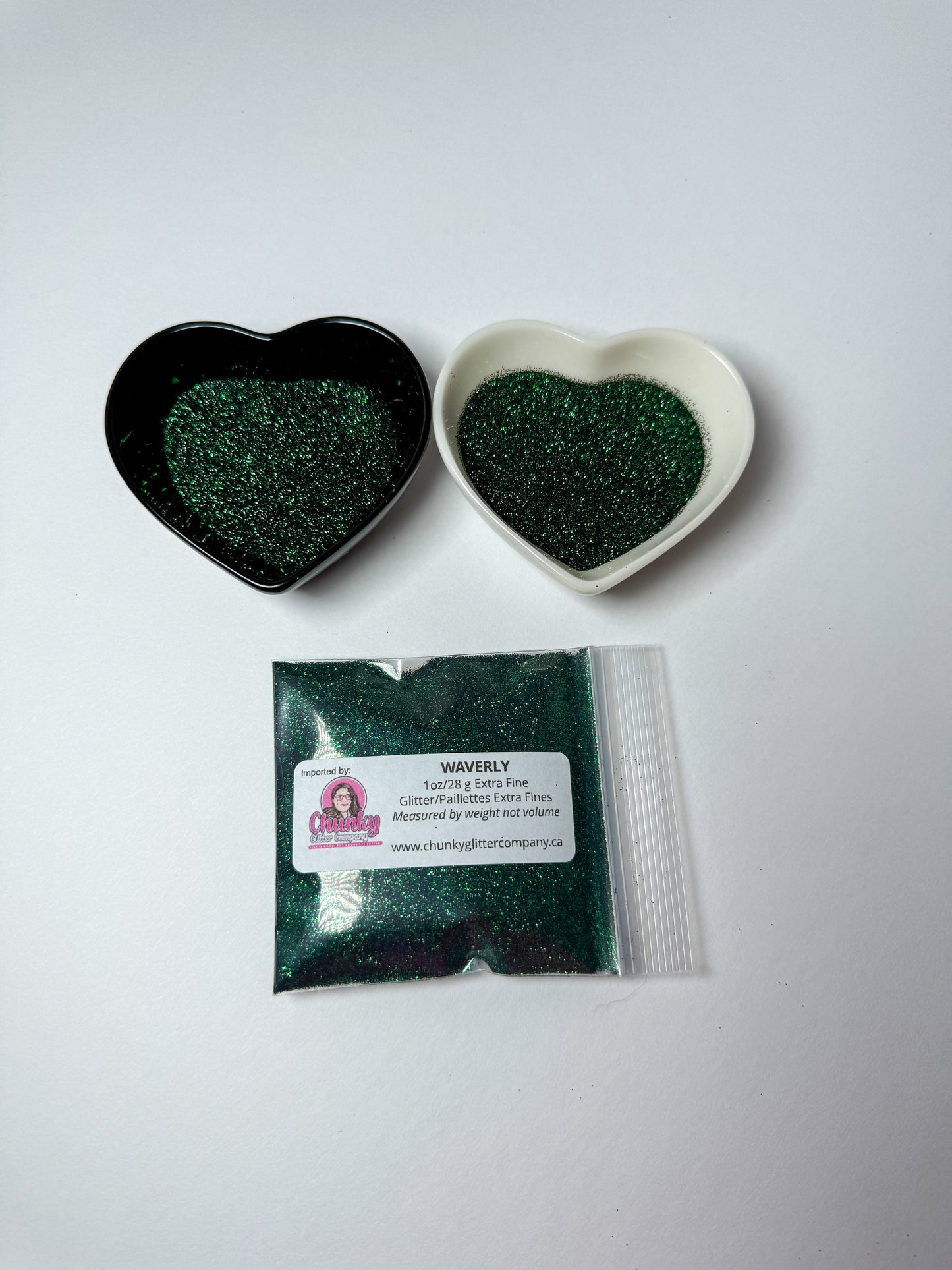 Two heart-shaped containers of glitter, one black and the other white, both showing an extra fine, dark green glitter mix and a bag of glitter with a label that reads Waverly.
