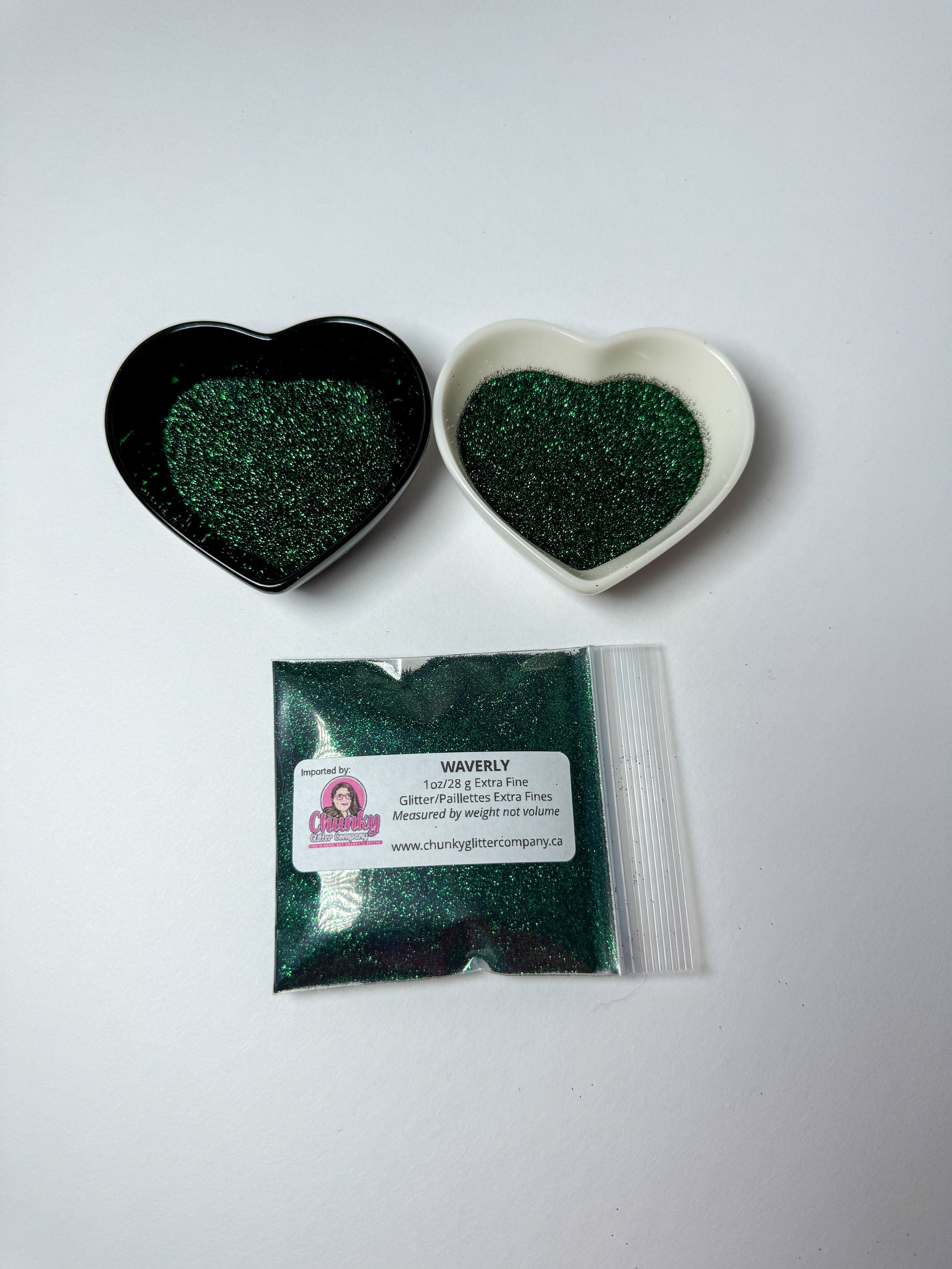 Two heart-shaped containers of glitter, one black and the other white, both showing an extra fine, dark green glitter mix and a bag of glitter with a label that reads Waverly.