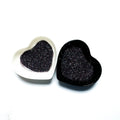 Two heart-shaped containers of glitter, one black and the other white, both showing an extra fine, multicolored glitter mix.