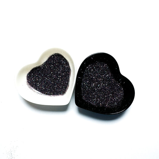 Two heart-shaped containers of glitter, one black and the other white, both showing an extra fine, multicolored glitter mix.