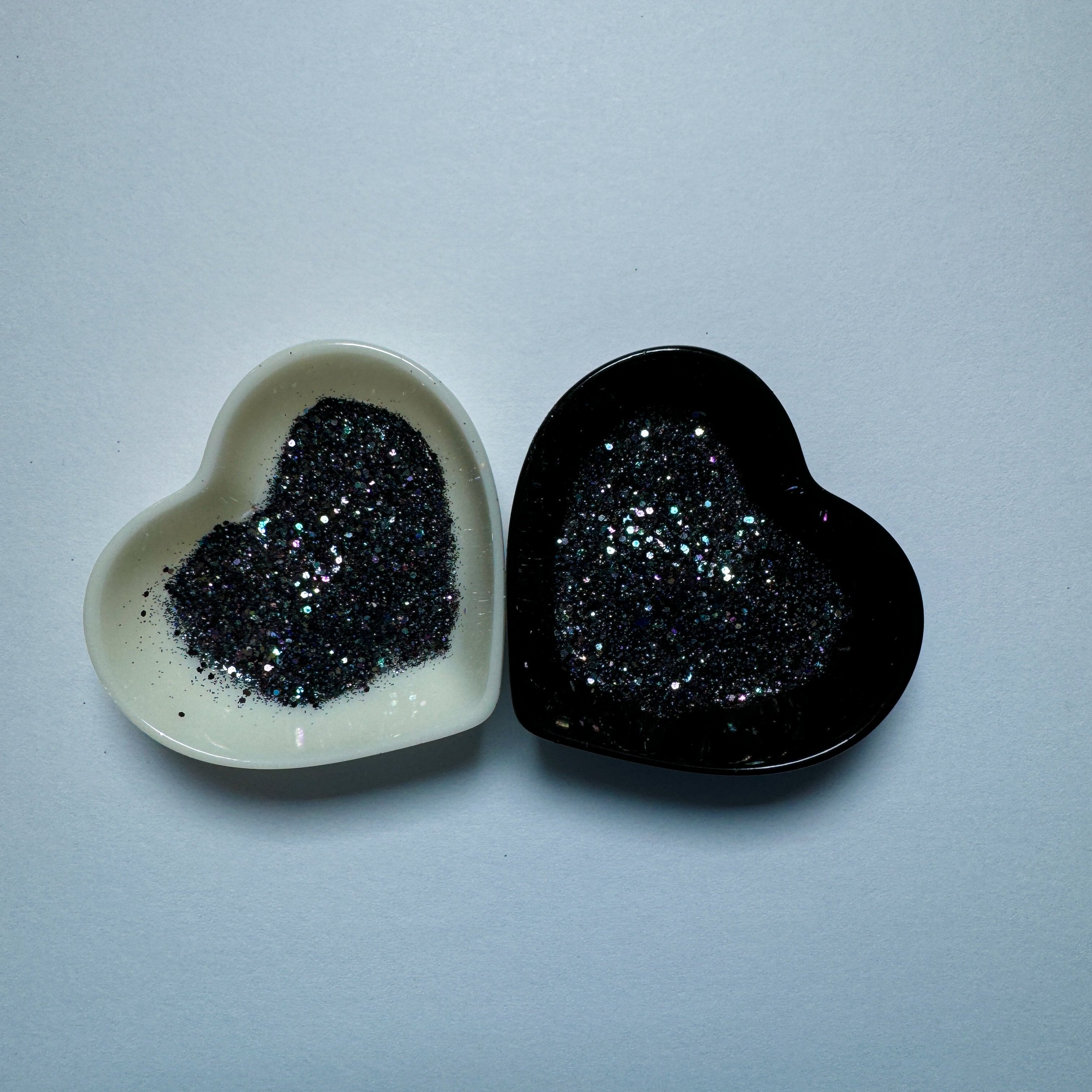 A white and black heart shaped dish showing a Black/Dark Purple/Dark Green medium glitter mix.