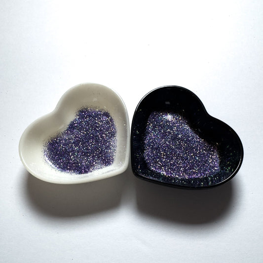 Two heart-shaped containers of glitter, one black and the other white, both showing an extra fine, blue, silver glitter mix.
