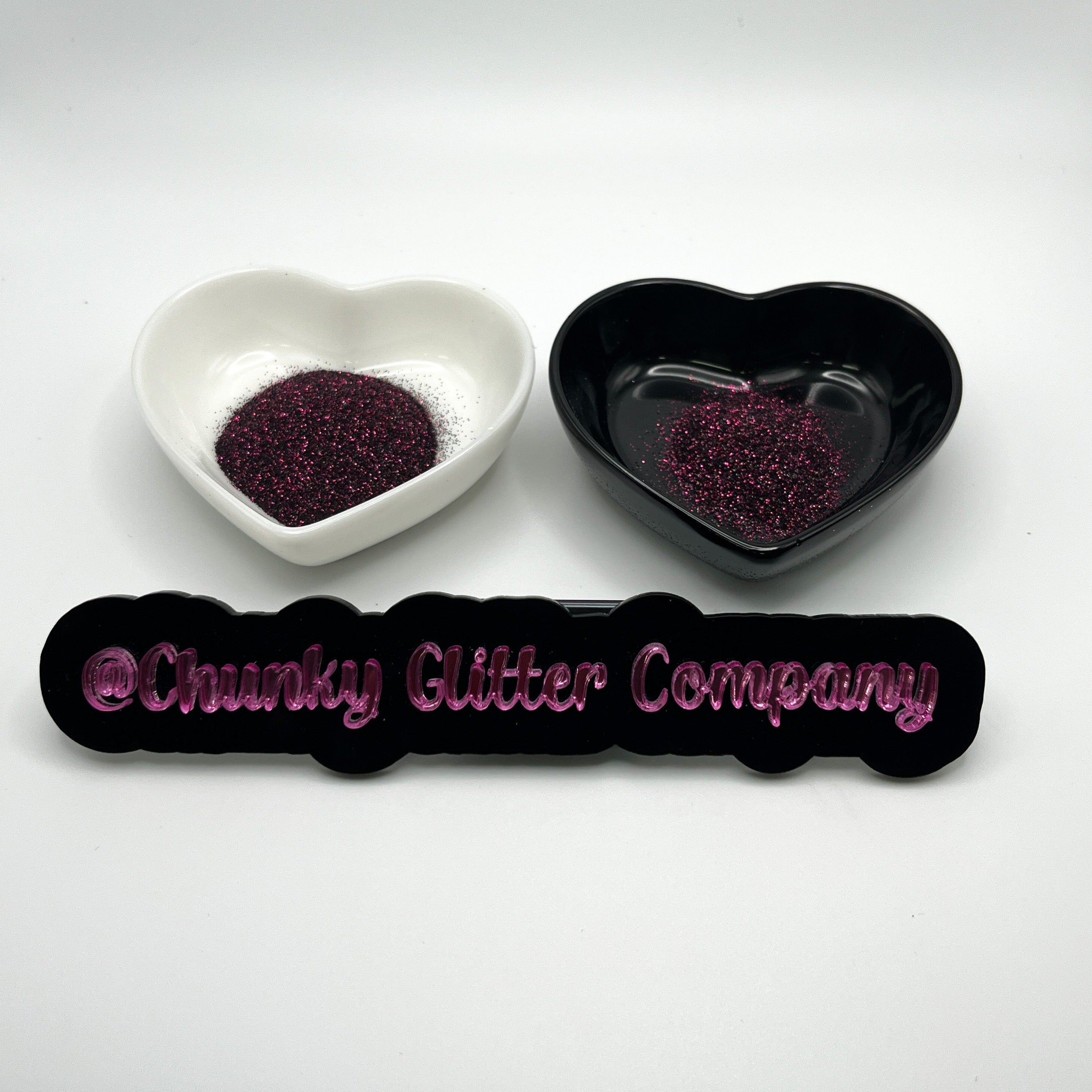 Two heart shaped containers, one black, one white, containing a dark extra fine glitter mix, with a label in front that reads '@ChunkyGlitterCompany'.