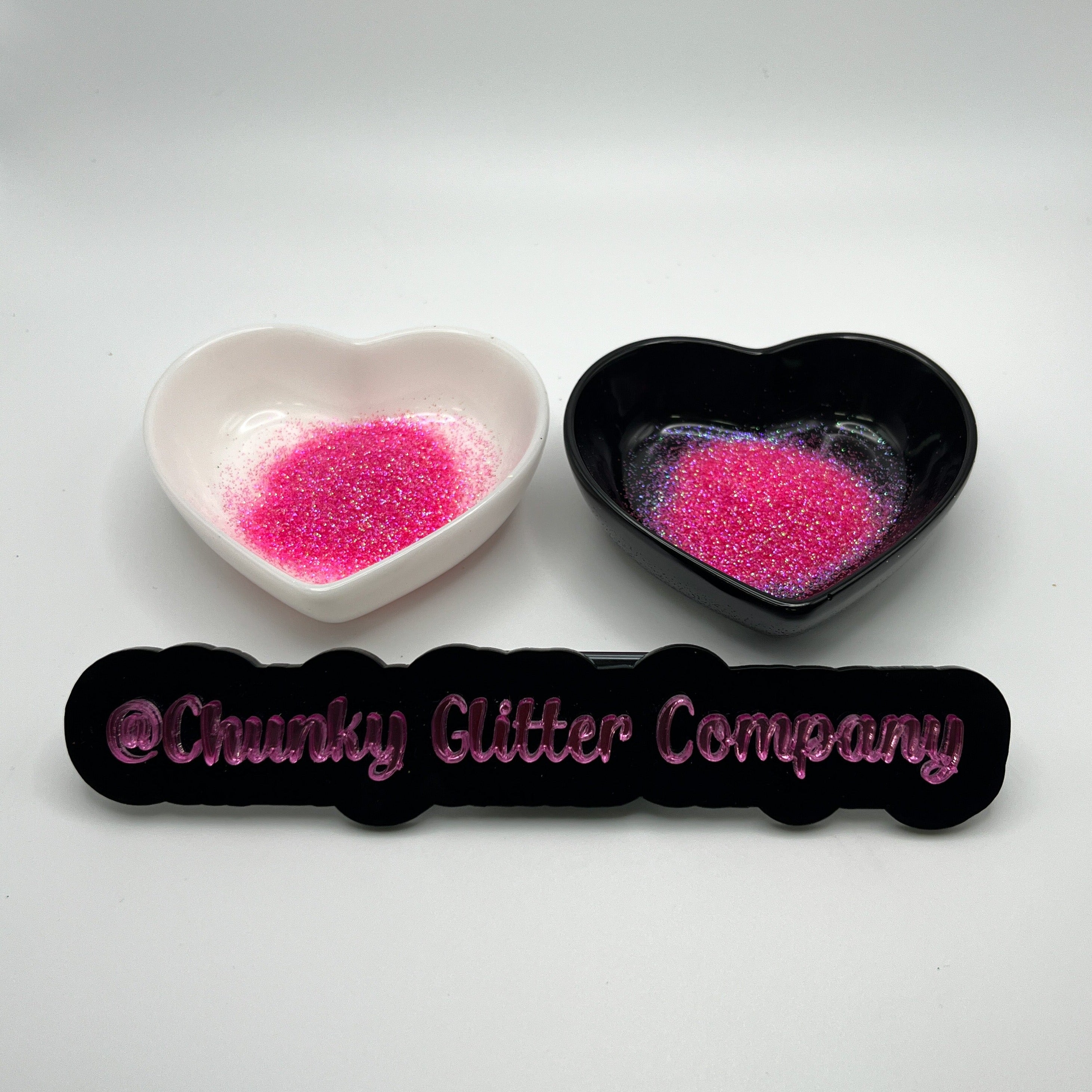Two heart shaped containers, one black, one white, containing a Pink extra fine glitter mix, with a label in front that reads '@ChunkyGlitterCompany'.