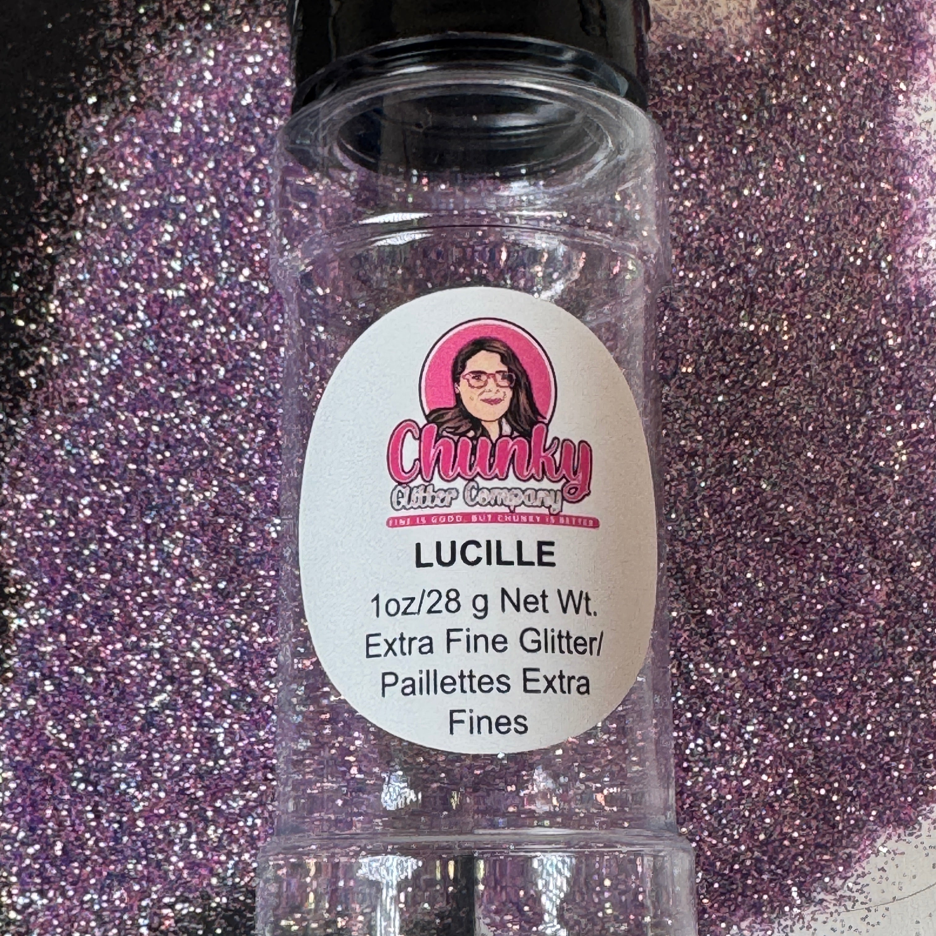 A clear plastic container labeled 'Lucille' filled with purple extra fine glitter, with the brand Chunky Glitter Company displayed on the label.