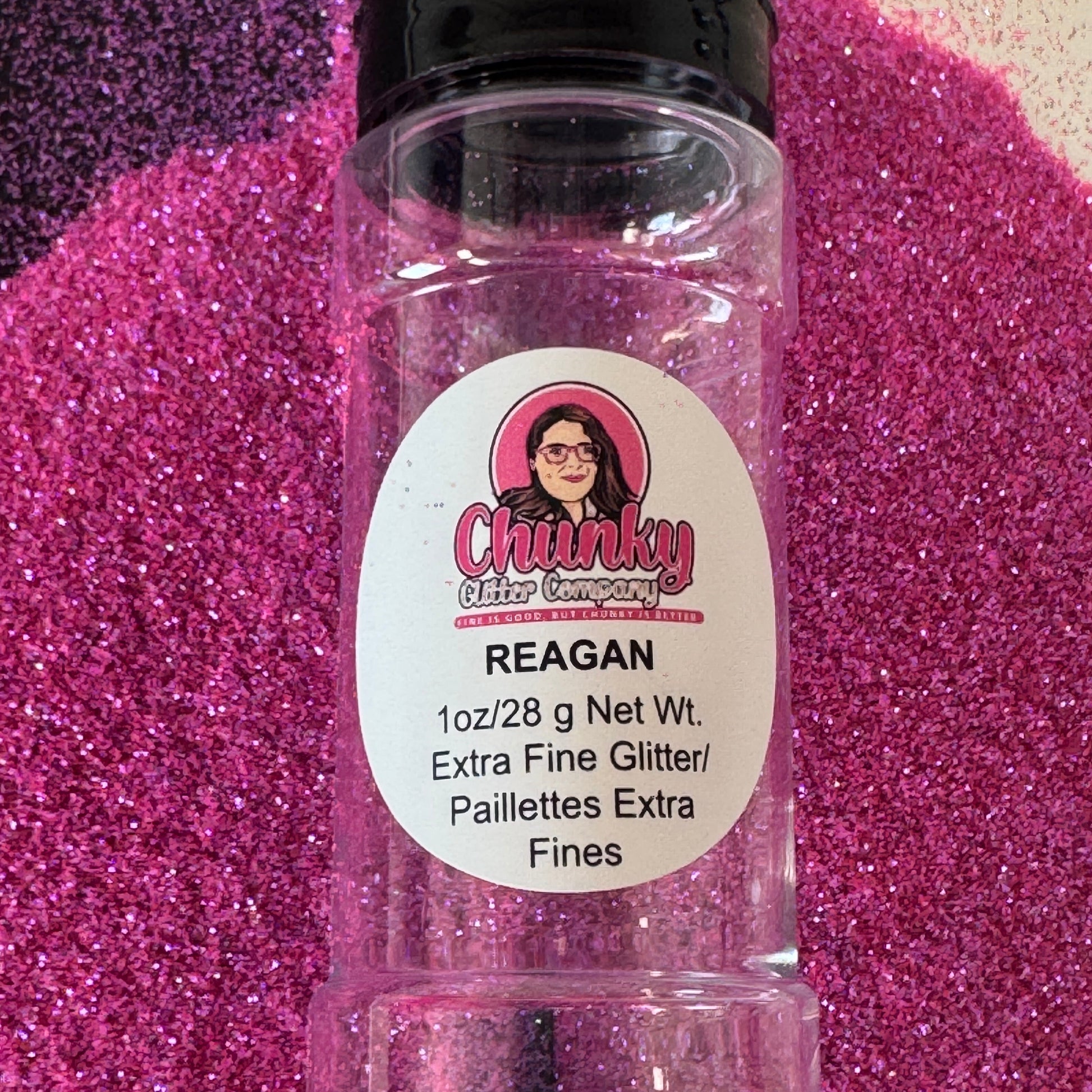 A clear plastic bottle of Reagan extra fine custom mix glitter, with a label showing the brand, product name, weight, and that it is solvent resistant polyester glitter.