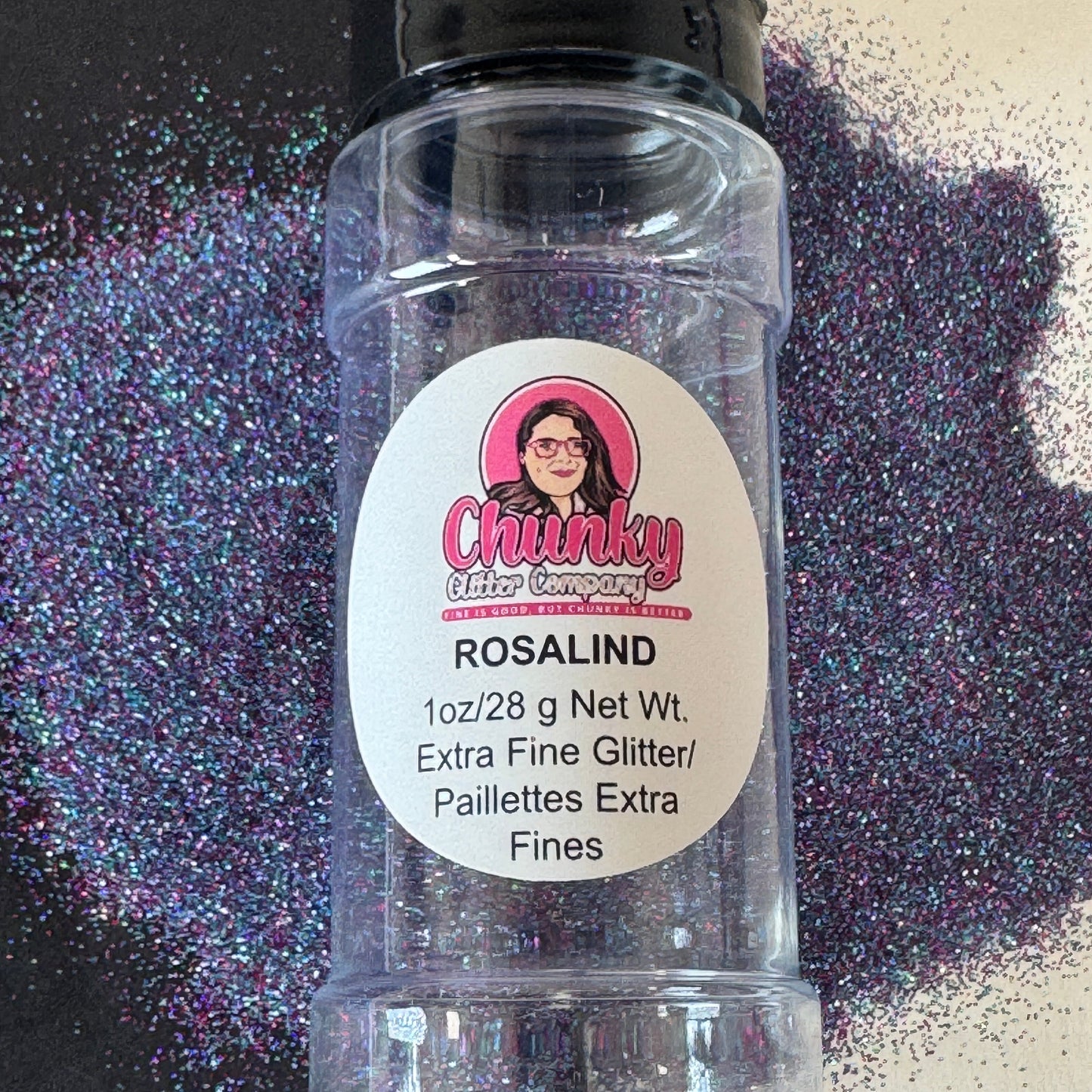 A clear plastic shaker bottle labeled 'Rosalind' containing extra fine blue mix glitter, with a black lid and a label featuring a pink logo and white text.