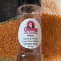 A clear plastic bottle with a black lid, labeled 'Chunky Glitter Company', containing extra fine glitter orange glitter mix with a scattered glitter background.