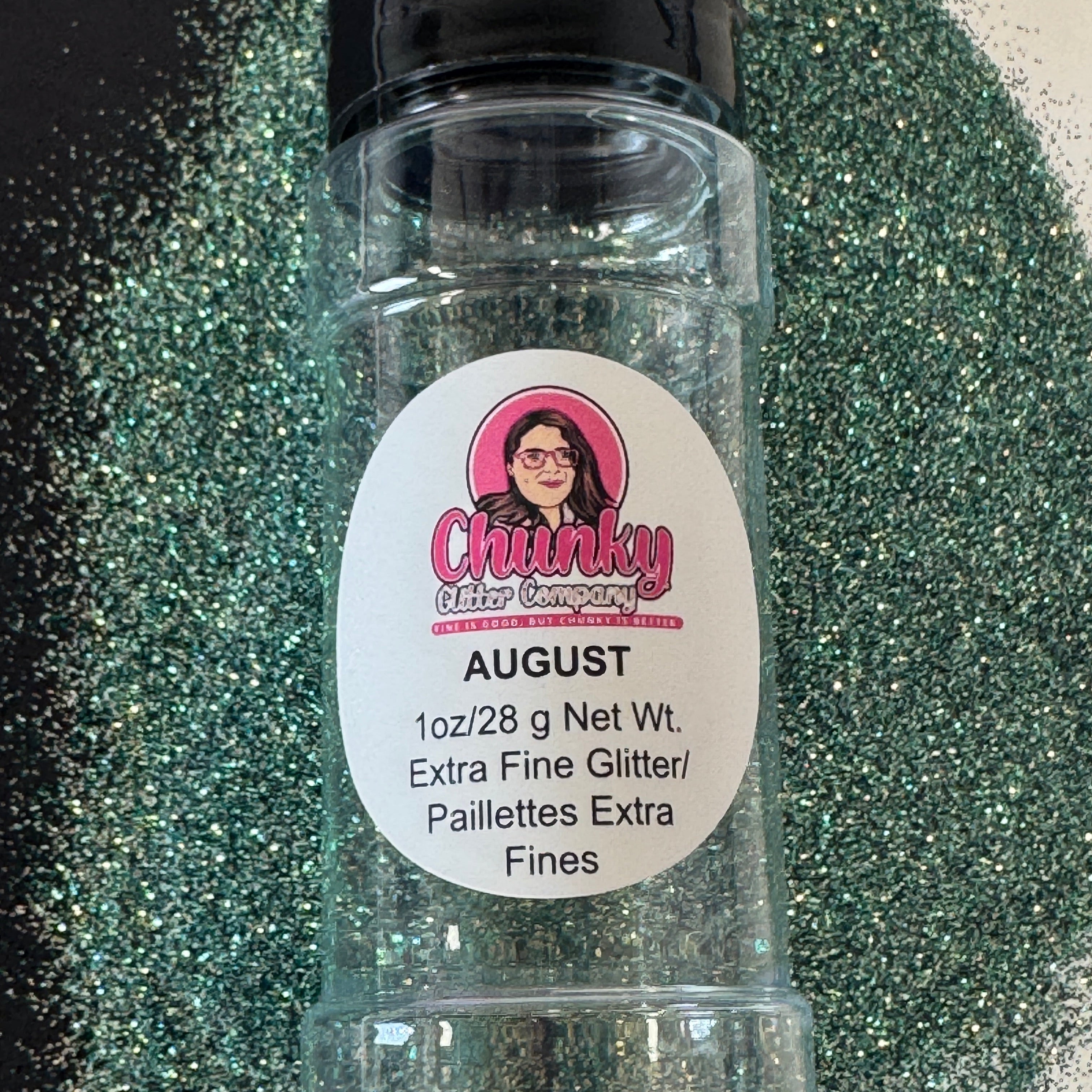 A bottle on top of a pile of turquoise and black glitter on a black and white background