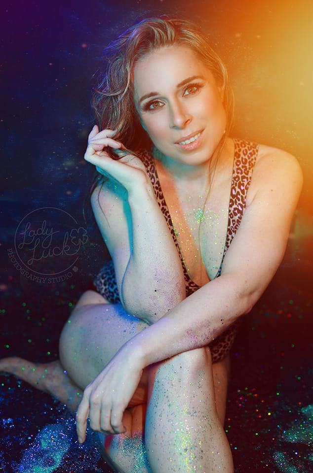 Woman in a leopard print outfit with colorful lighting effects showing off glitter on her skin