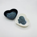 Two heart shaped containers, one black, one white, containing a dark extra fine glitter mix.