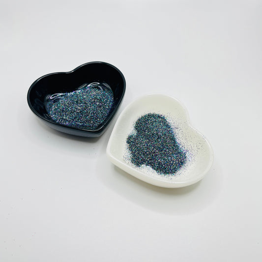 Two heart shaped containers, one black, one white, containing a dark extra fine glitter mix.
