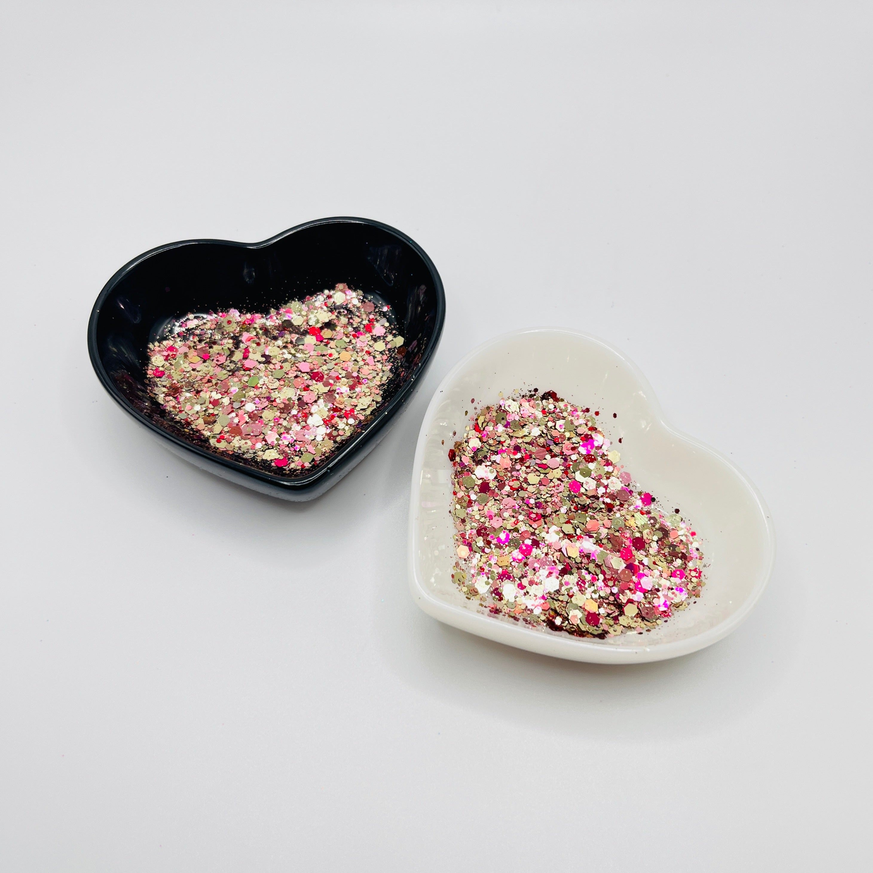 Two heart shaped containers, one black, one white, containing a Gold/Pink/Light Pink chunky glitter mix.