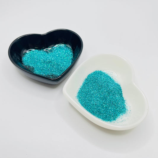 Two heart-shaped dishes, one black and one white, containing blue polyester glitter.