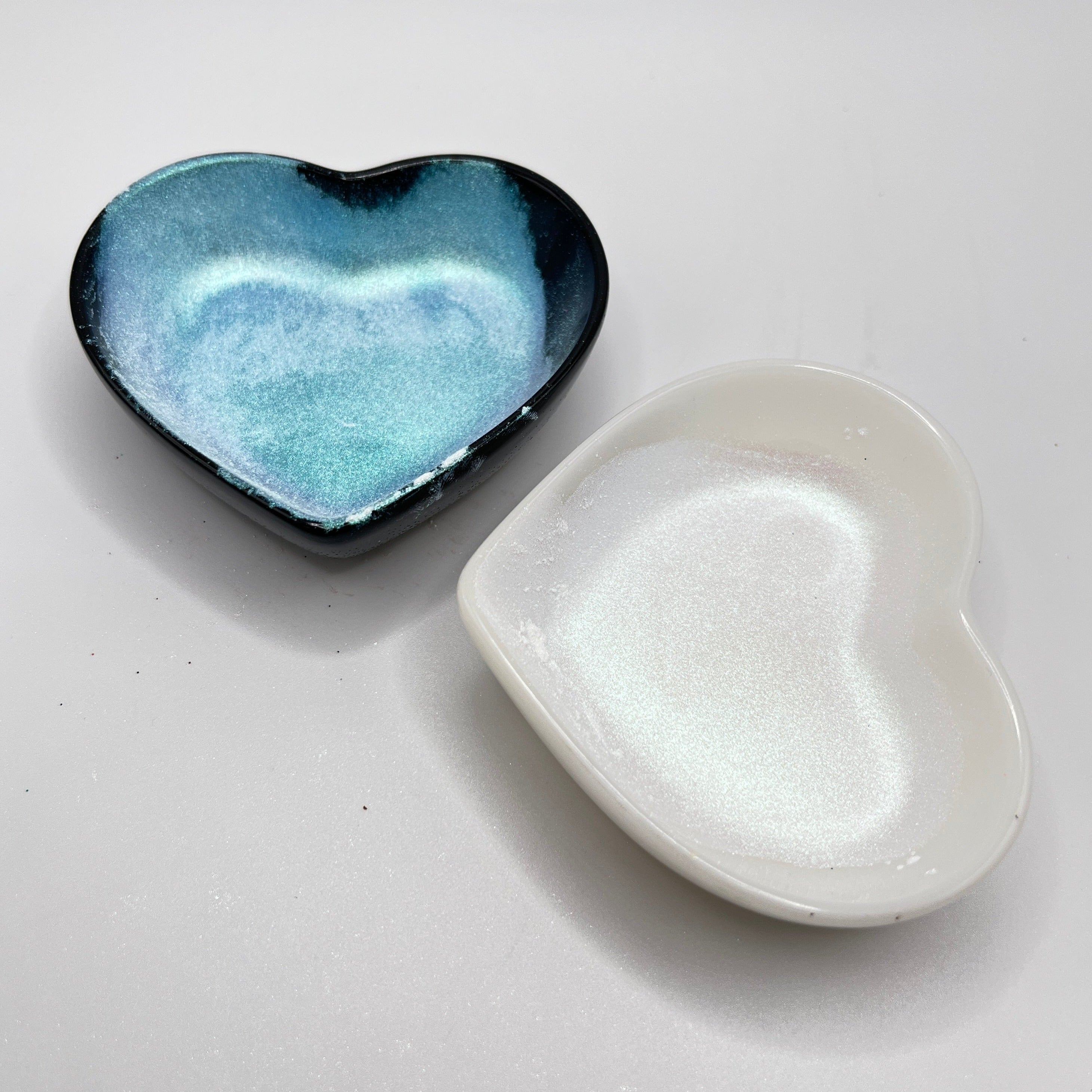 Two heart shaped containers, one black, one white, containing a white chameleon mica powder.